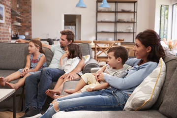 Family Sit On Sofa In Open Plan Lounge Watching Television
