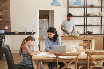 Mother Helps Daughter With Homework As Father Makes Meal