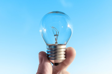 Concept idea of a burning incandescent lamp in a hand against a clear blue sky background from...