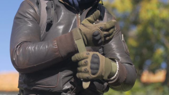 A man in a brown leather jacket securing his motorcycle riding gloves