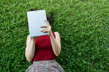 Woman lay down on green grass and using tablet