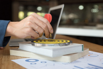 Businessman 's hand holding dart hitting at the business target on dartboard on desk in office. ...