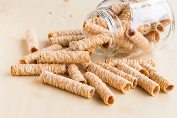 Crispy rolled wafer sticks, traditional dessert in Thailand, are collocated on the wood board outside a bottle.