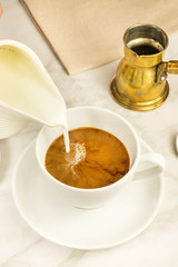 Milk poured into cup of coffee, diner's perspective
