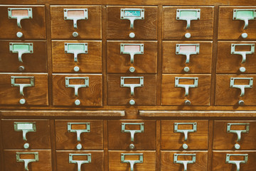 An old style wooden cabinet of library card  or file catalog index drawers with label holders and blank labels facing front