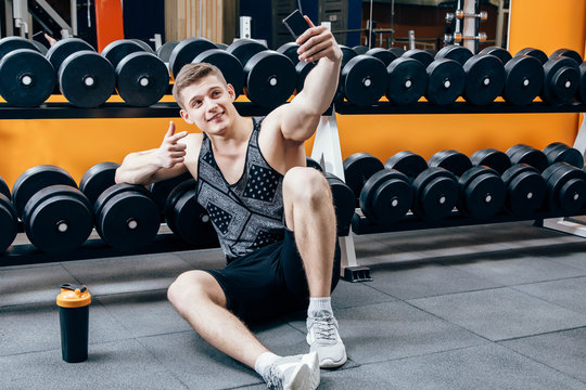 Image of happy young sportsman sitting in gym and make selfie.