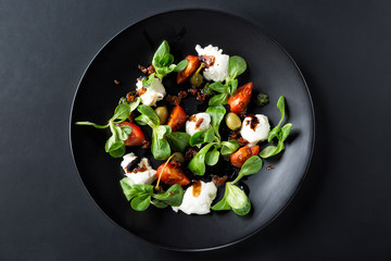 Caprese salad with mozzarella, tomato, basil and balsamic vinegar arranged on black plate and dark background. Top view