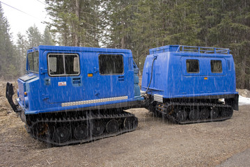 small snowcat with second wagon attached to the trailer coupling, electric blue, used to transport people in mountain huts, photographed in early spring, during a light snowfall, Trentino Alto Adige, 