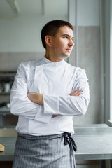 Young male chef posing with hands crossed at kitchen. 