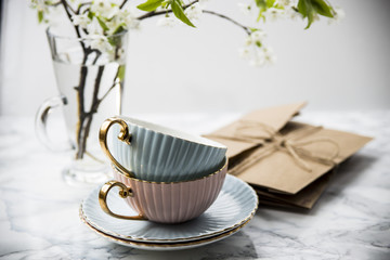 Letters in craft envelopes with a bow on a marble table next to tea cups and a vase with spring flowering branches