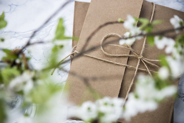 Letters in craft envelopes with a bow on a marble table next to tea cups and a vase with spring flowering branches