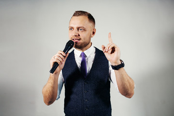 The entertainer. Young elegant talking man holding microphone, Isolated on grey background