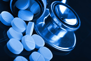 Medical pills loose from the bottle next to a stethoscope
