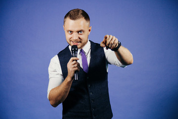 The entertainer. Young elegant talking man holding microphone, Isolated on blue background
