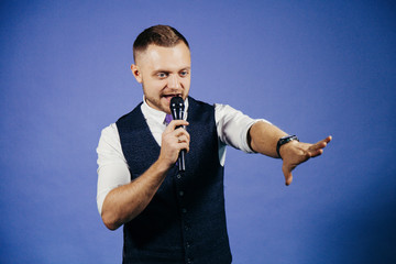 The entertainer. Young elegant talking man holding microphone, Isolated on blue background