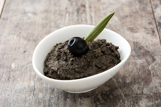 Black olive tapenade with anchovies, garlic and olive oil on wooden background

