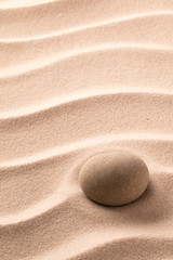Fototapeta na wymiar Round stone laying on rippled beach sand. Zen meditation minimalism. Concept for relaxation and concentration.