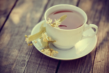 On a wooden table a cup of tea with lime flowers.