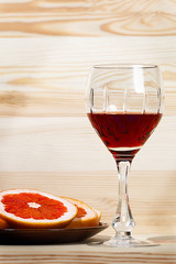 Wine in a glass stands on a wooden background, next to a plate with sliced grapefruit