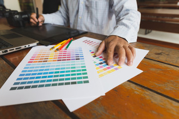 freelance graphic designer using digital tablet, computer, man working with color swatch catalog samples for selection - Creativity Editor Ideas Designer Concept