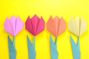 Origami bright colored tulip flowers on a yellow background.