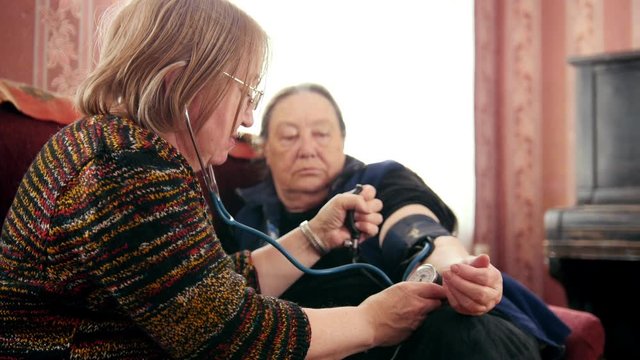 Two senior ladies checking health state with manometer - measures pressure, pensioners