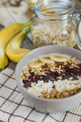 Oatmeal with bananas, cranberry, chia seeds, coconut shreds, almonds. Healthy breakfast concept. Rustic wooden background.