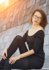 Fototapeta premium Beautiful young woman in black posing next to a stone wall