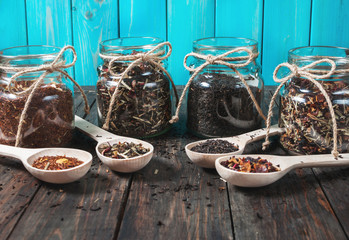 Different kinds of tea in jar and wooden spoons on wood table