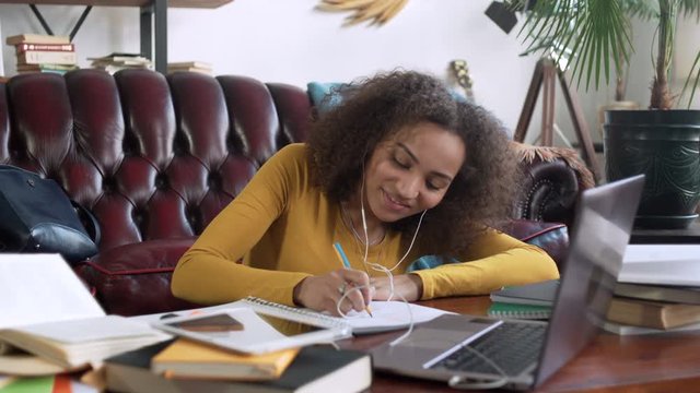 young african woman take part in video call using app on laptop computer for education online and remote working discussion making notes in notebook sitting on floor near sofa at home during sunny day