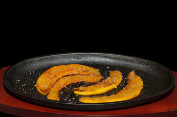 Roasted chunks of pumpkin in vegetable oil with spices in a cast iron skillet. Black background.