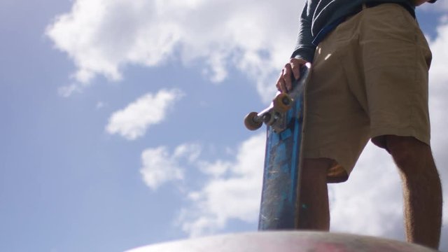 Legs of a skateboarder holding onto his board on top of a ramp, in slow motion