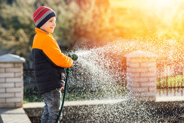 Little boy watering flowers with sunset background
