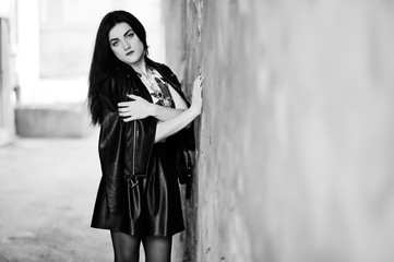 Young goth girl on black leather skirt and jacket against grunge wall.