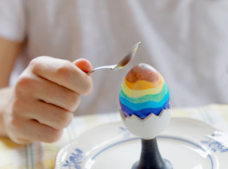 Closeup of a the hand of a man in white shirt starting to eat a painted colorful Eastern egg with a spoon