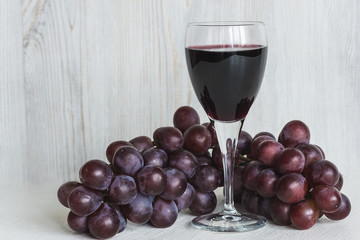 glass of red wine and grapes on light wooden background