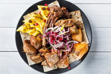 Lyulya kebab, shish kebab, grilled salmon fish, onion and pomegranate grains on black plate and white wooden table. Top view