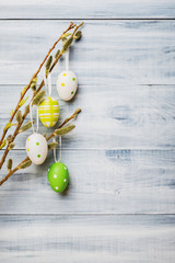 Easter eggs hanging on willow branches over white wooden background