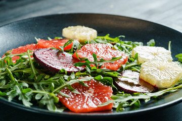 Fresh mix salad of red beet, grapefruit and orange on a cushion of arugula in a black dish. Closeup view.