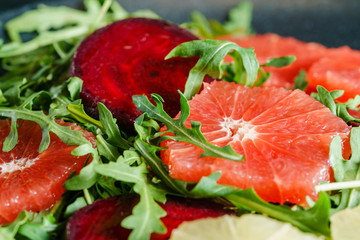 Fresh mix salad of red beet, grapefruit and orange on a cushion of arugula in a black dish. Closeup view.