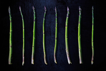 Green purple asparagus in a row on a dark background