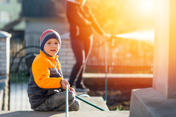 Little boy help mother with watering flowers, sunset