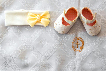 Christening details. On white baby shoes and bandage. Golden cross on a white canvas