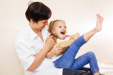 Beautiful brunette woman showing a book to her baby while sitting on a bed in her apartment