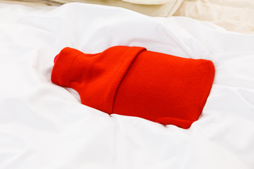 Warm red hot water bottle on white bedding