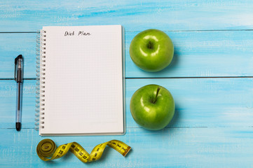 Healthy eating, dieting, slimming and weigh loss concept - close up of diet plan paper green apple, measuring tape. Copy space for text 
