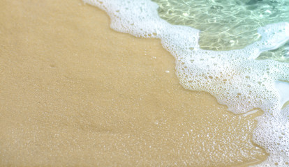Soft wave with foam on the sandy beach.