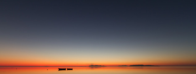 A warm sunset on a calm water, with Islands in the background - obrazy, fototapety, plakaty