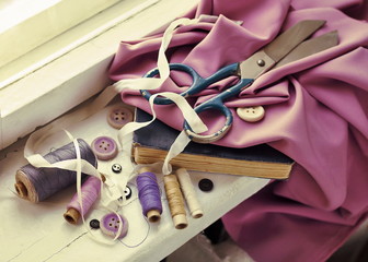 Old scissors, spools of thread, fabric and buttons on the windowsill. 