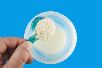 Male hand pours spoonful protein powder into the shaker bottle with milk, on blue background, cooking a protein shake, sports nutrition, top view